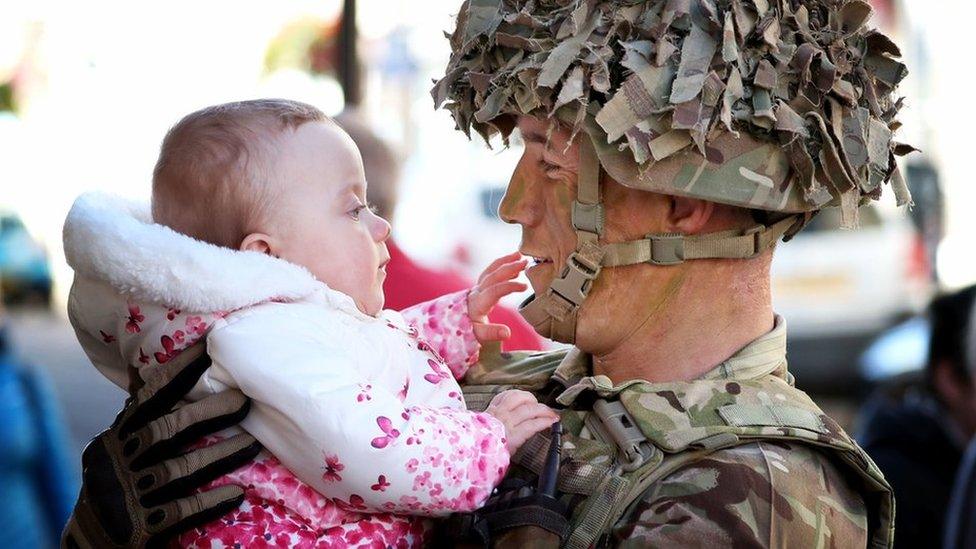 A soldier holds his baby as they look at each other