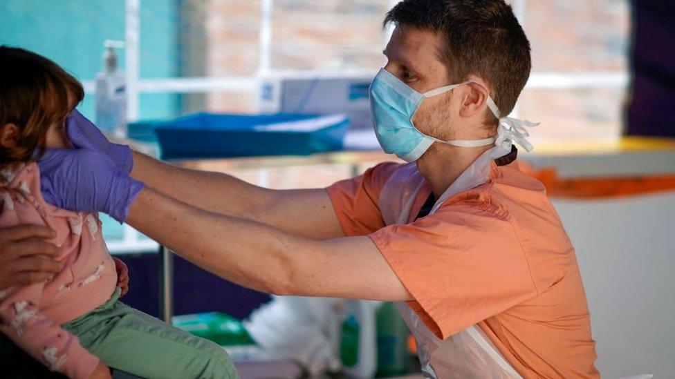 A doctor tends to a child while dressed in full PPE equipment.