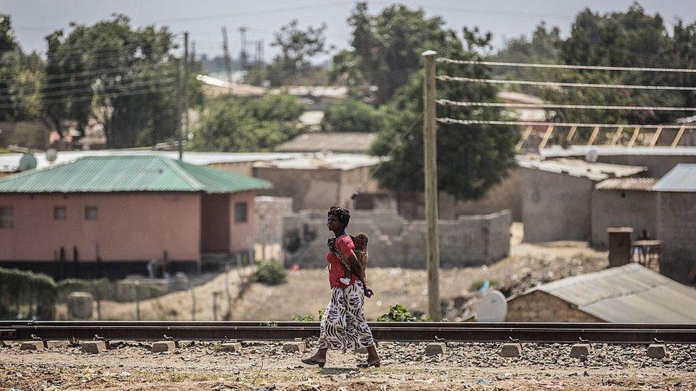 A woman walks with her baby on her back on the oustkirts of Lusaka, Zambia