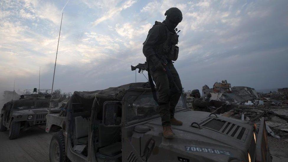 An Israeli soldier standing on the hood of a military vehicle at a position in the Palestinian town of Beit Lahia, on the outskirts of Gaza City, northern Gaza Strip, 8 December 2023