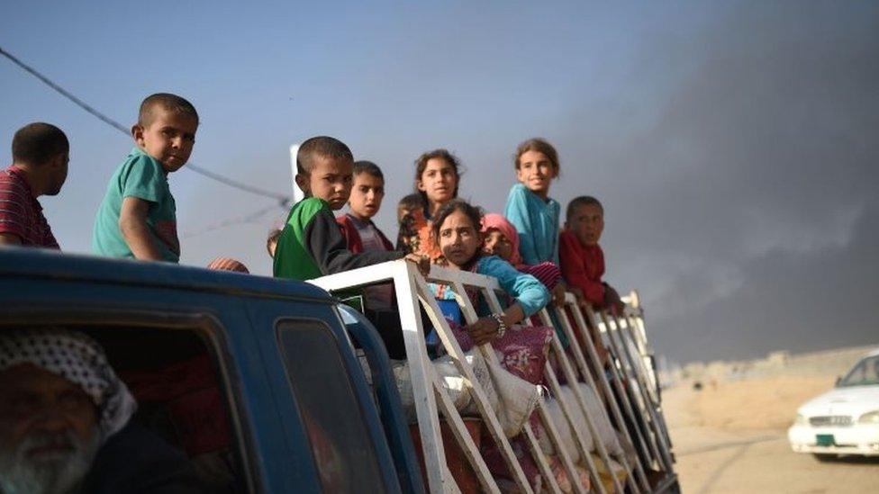 Displaced Iraqis stand on the back of a pick-up truck as they arrive to a refugee camp in the town of Qayyarah, south of Mosul (22 October 2016)