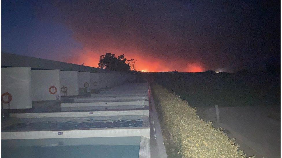 A red glow in the sky, hotel in the foreground.