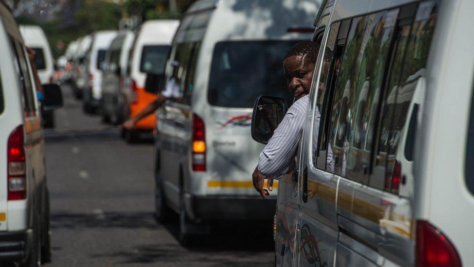 Minibus taxis line up a road with a driver looking out his window