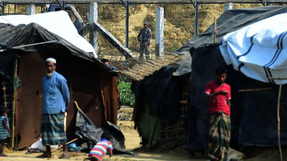 A Myanmar security personnel keeps watch along the Myanmar-Bangladesh border as Rohingya refugee stand outside their makeshifts shelters near Tombru