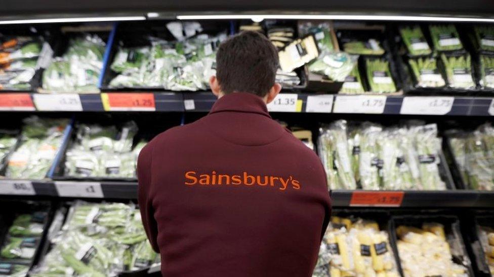 A Sainsbury's worker stacks a vegetable shelf in a store