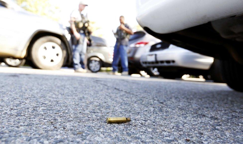 A gun cartridge lies on the ground near a car