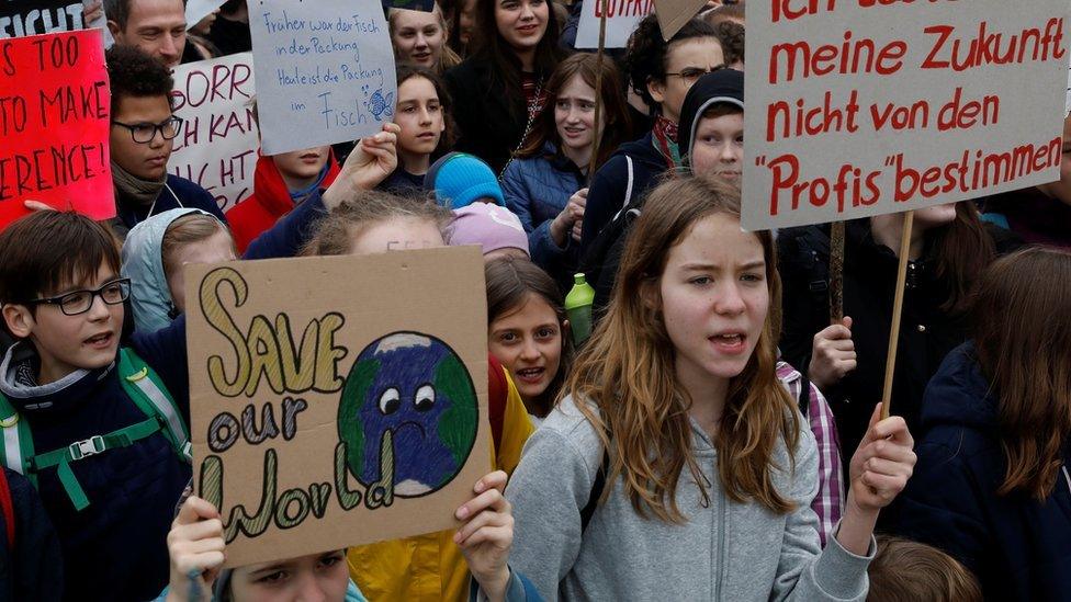 School-aged children and young teenagers wave placards with German and English text in this crowd shot