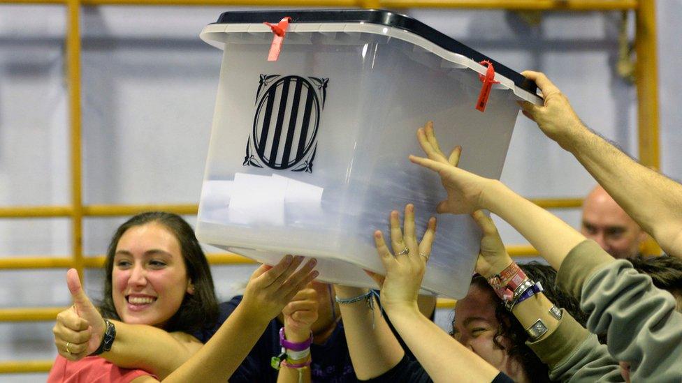 People smiling hold aloft a ballot box, shut and sealed with anti-tamper ties, as they celebrate the end of polling day