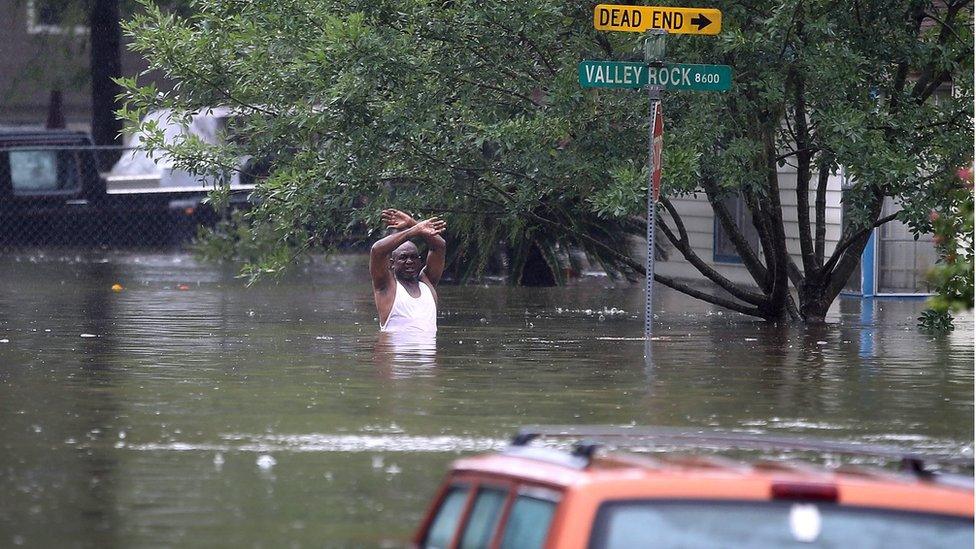 A man stands in chest-deep water on a flooded street in Houston.