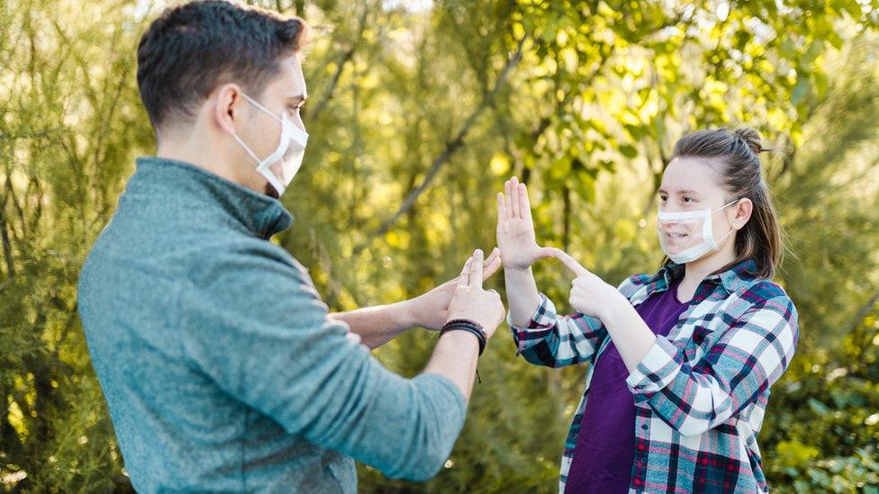 Two people wear clear masks and use sign language