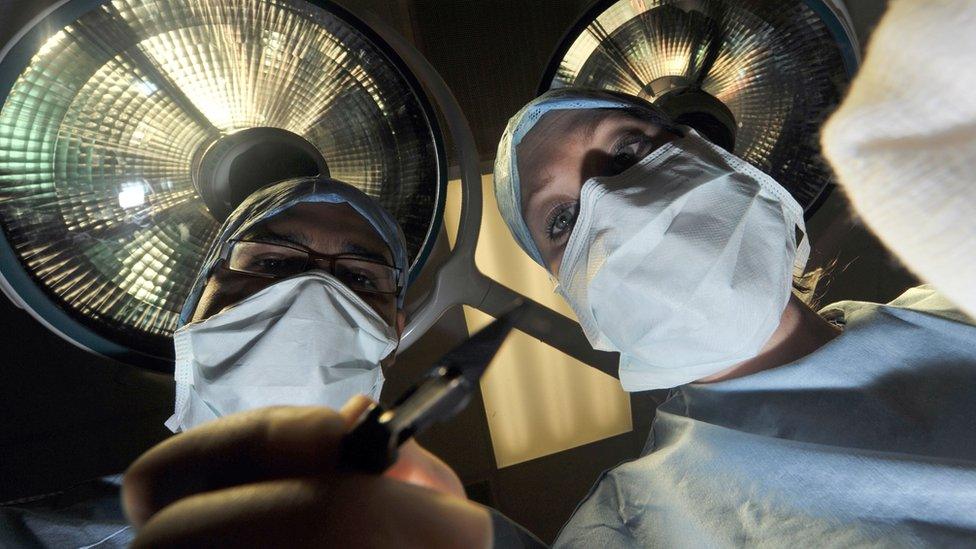 A theatre nurse and a surgeon holding a scalpel perform an operation