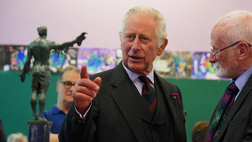 Prince Charles seen pointing at a statuette while meeting people on a visit to a food bank