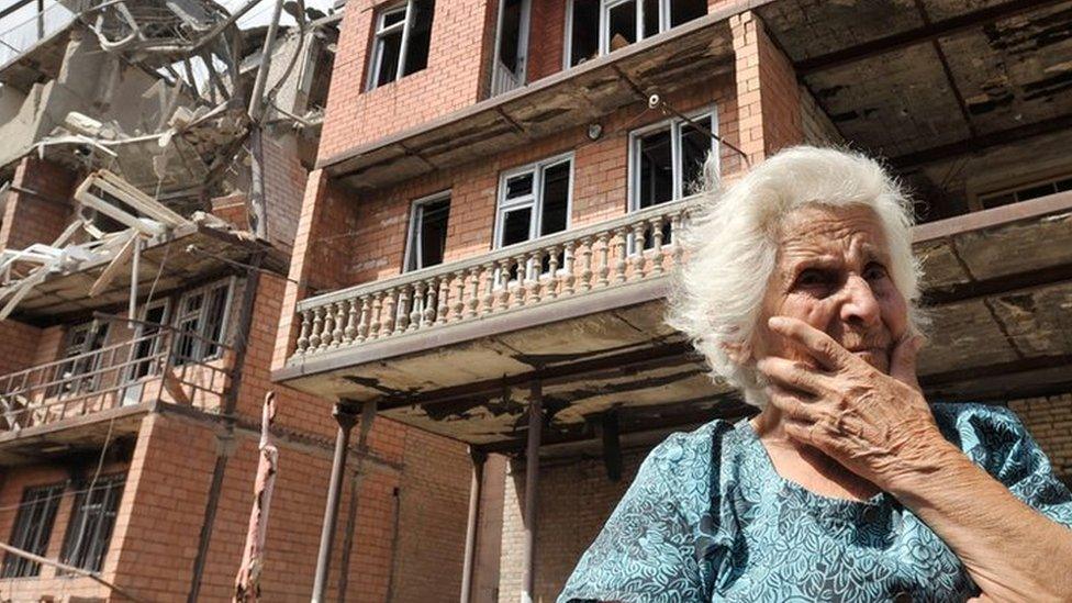 a Georgian woman in front of her home, which has been destroyed