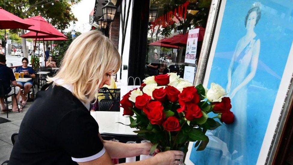 A woman places roses in front of a picture of the Queen, outside a restaurant in California, USA.