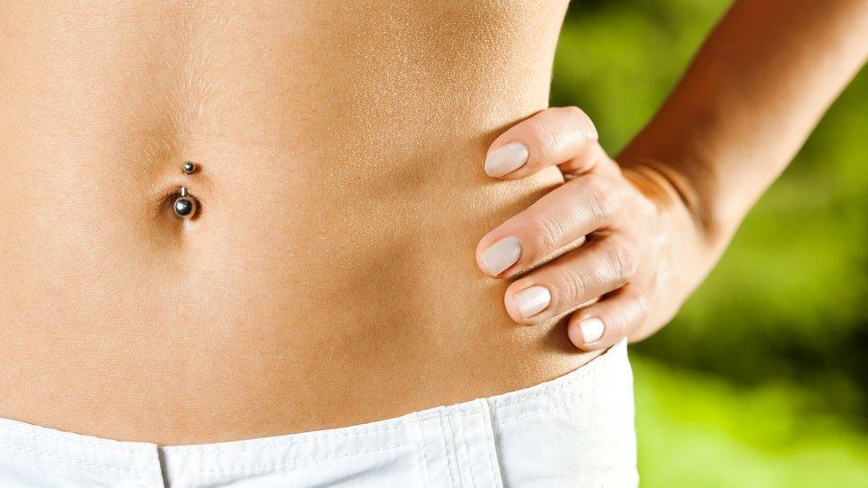 A woman's stomach - she is wearing a belly button bar