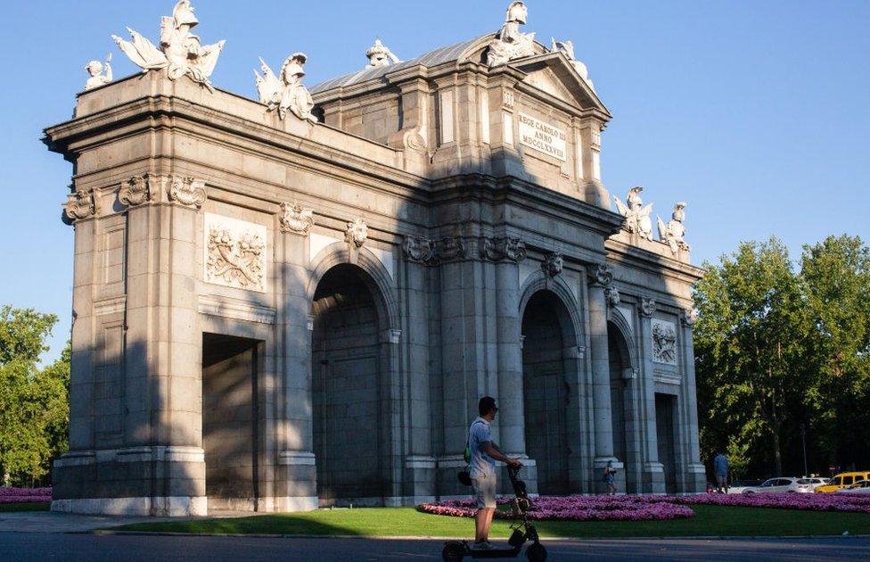 A man rides an electric scooter in front of the Puerta de Alcalá in Madrid