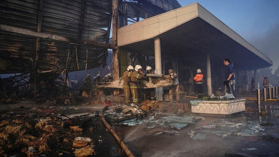 Rescuers in firefighting gear work at a site of a shopping mall hit by a Russian missile strike