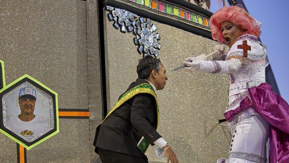 A man dressed as a president being jabbed by a person dressed as a nurse