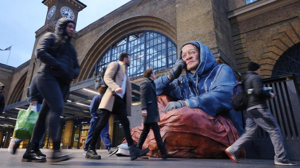 Commuters looking up at the sculpture at King's cross station as they pass by on their journeys.