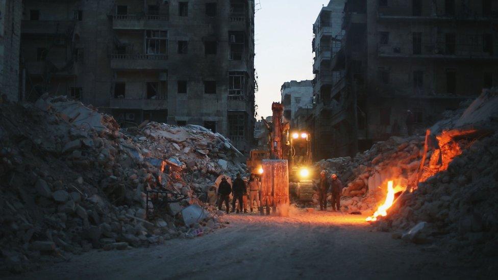 A digger lit up in the rubble in Aleppo