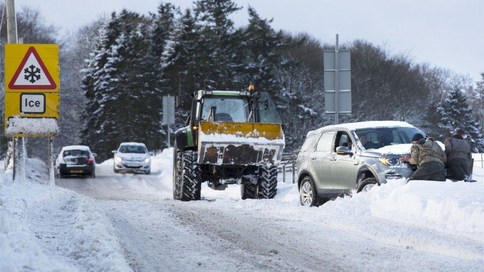 Drivers help to push a vehicle back on the road after heavy snow made road conditions difficult in Midlothian near Edinburgh