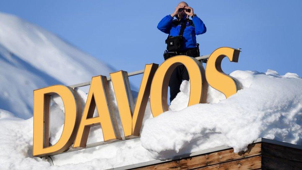 Swiss armed security personnel stand guard on the rooftop of a hotel, next to letters covered in snow reading Davos