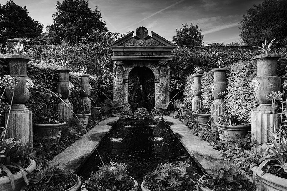 Stone water fountains pour water into a pond in a leafy garden