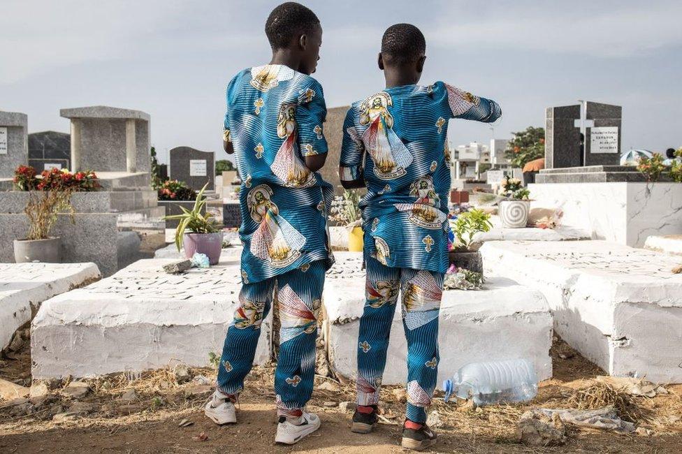 Two boys in matching batik outfits stand in front of a grave.