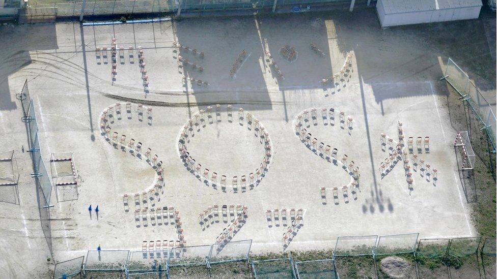 Sign words formed by chairs reading "(Toilet) paper, bread, water and SOS" are seen on a playground at Kumamoto Kokufu High School