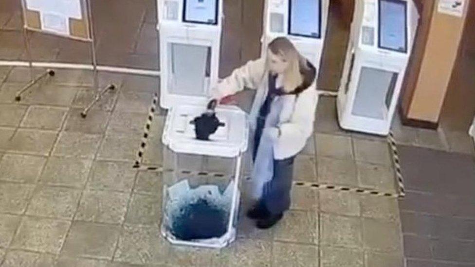 A woman pours a liquid into a ballot box, during the Russian presidential election in Moscow, Russia, in this screen grab taken from a video recording of a screen showing CCTV footage, March 15, 2024