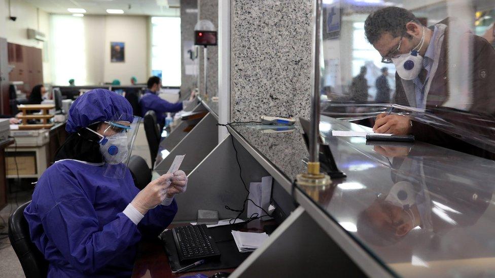 A bank employee wear protective masks in Tehran, Iran (17 March 2020)