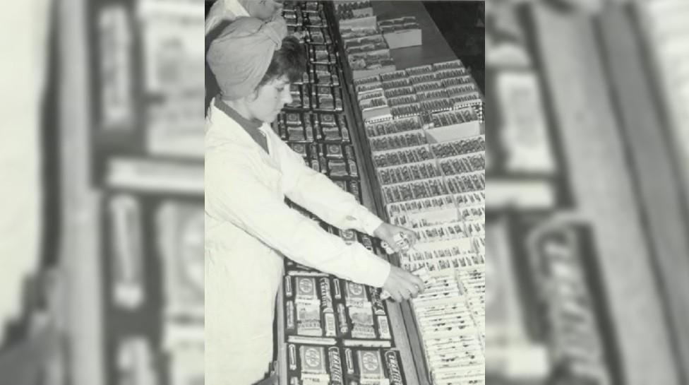 A woman puts together a selection box of confectionery, wearing a pristine white overall