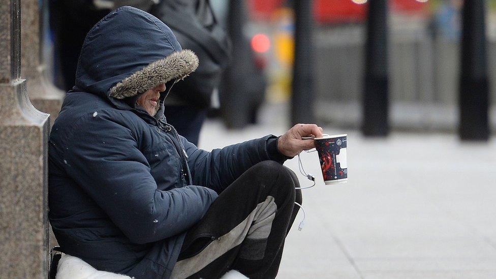 A file photo shows a homeless man sat on a street holding out a paper cup