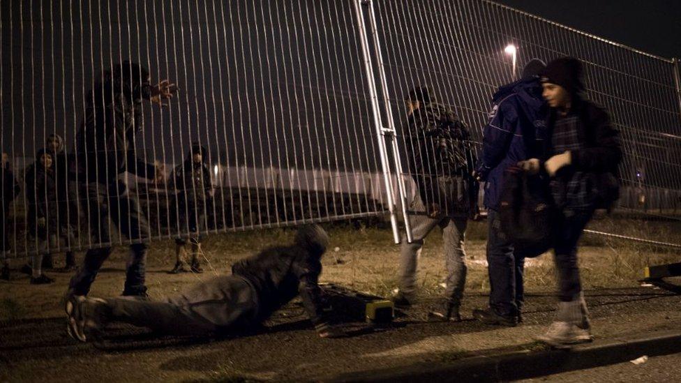 Migrants climb under a fence