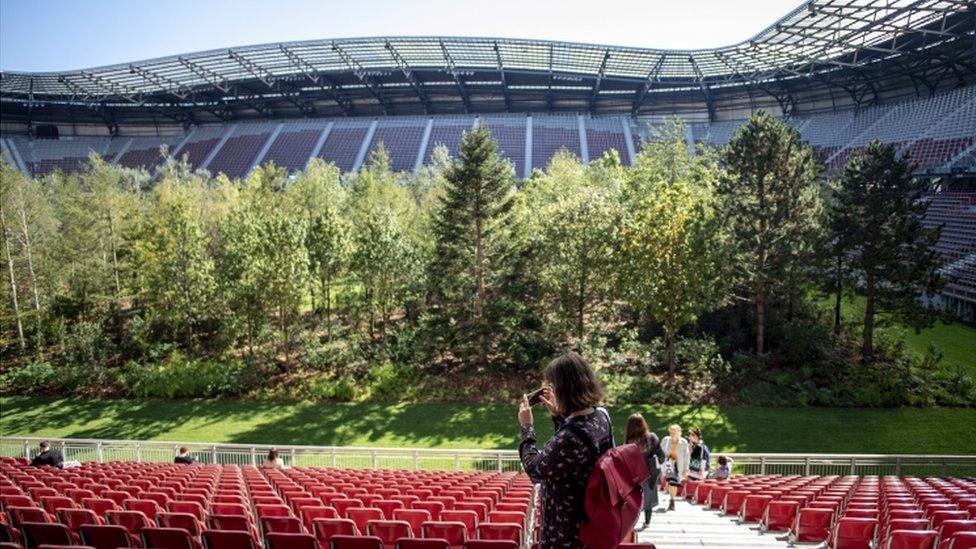 A woman takes a photo of the forest from the seats of the stadium