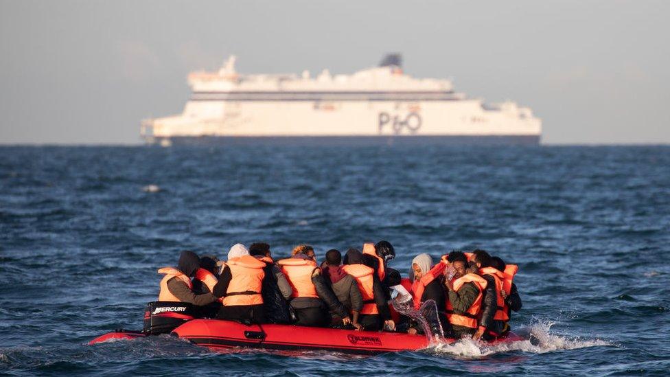 Migrants cross the channel with a ferry in the distance.