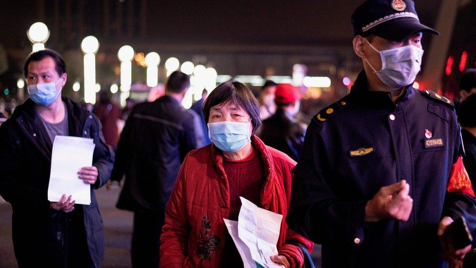 Passengers wear facemasks as they form a queue at the Wuhan Wuchang Railway Station in Wuhan, early on April 8, 2020