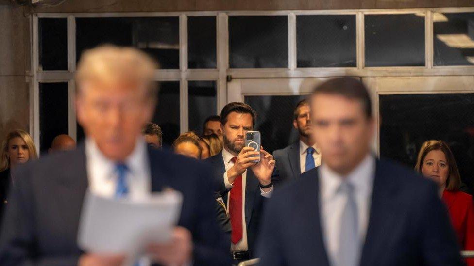 Senator JD Vance takes a photo as Donald Trump and his lawyer speak during a break in his criminal trial