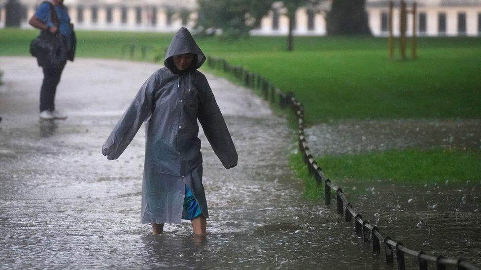 A woman wades through a flooded path in St James's Park in central London