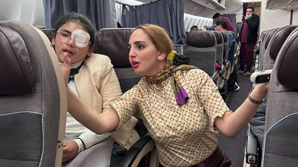 A member of the aircrew explains the plane's entertainment system to a Palestinian girl with an eyepatch