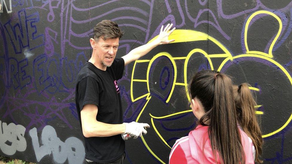 Donal O'Doherty teaching a girl how to spraypaint