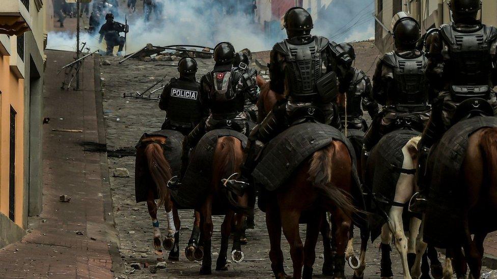 About 10 police on horseback marching through the hilly streets of Quito