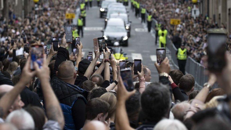 People taking photos with their phones of the funeral procession.