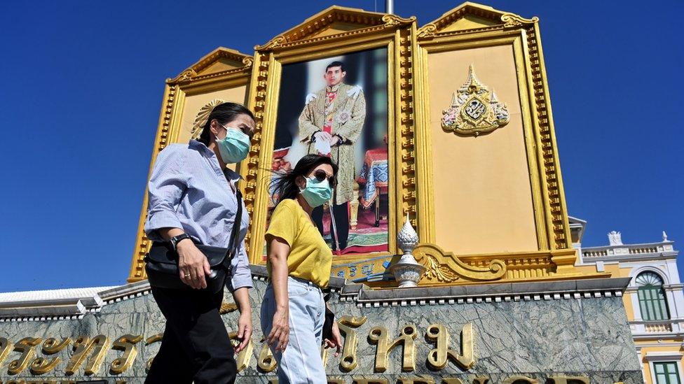 People with face masks walk pass a large portrait of Thailand's King Maha Vajiralongkorn near the Grand Palace in Bangkok on January 27, 2020