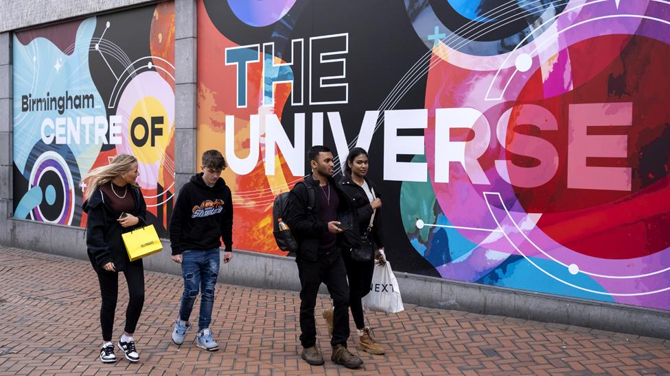 People in the city centre pass by a large scale poster advertising the city of Birmingham on 22nd March 2023 in Birmingham, UK