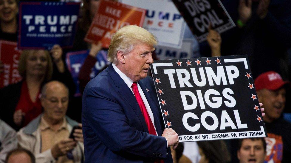 Donald Trump holds a sign reading "Trump digs coal" at an election campaign rally in 2016