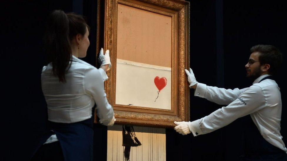 Sotheby's employees pose with the newly completed work by artist Banksy entitled "Love is in the Bin", a work that was created when the painting "Girl with Balloon" was passed through a shredder in a surprise intervention by the artist, at Sotheby's auction house in London on October 12, 2018, following the work's sale.