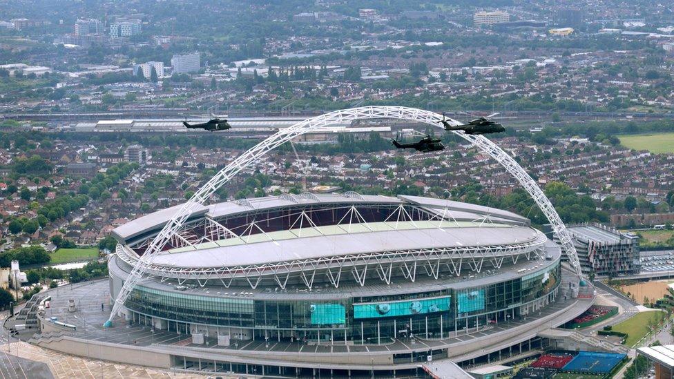 Aerial picture of Wembley Stadium with helicopters flying past.