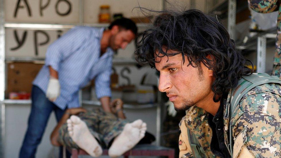 A Syrian Democratic Forces (SDF) fighter sit as medics treat his comrades injured by sniper fire by Islamic State militants in a field hospital in Raqqa, Syria, 28 June