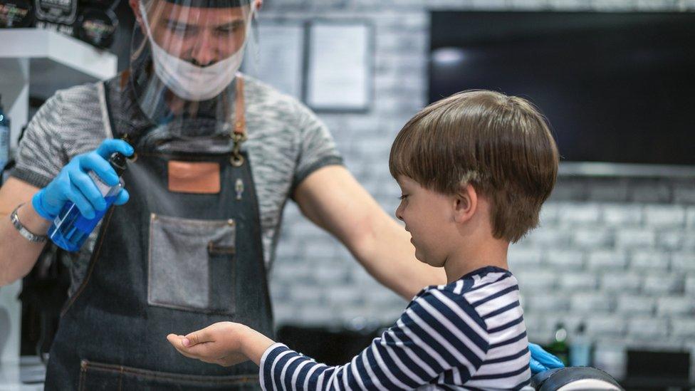 A hairdresser spraying sterilising fluid onto a boy's hands